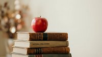 Red apple resting on stack of vintage books with natural philosophy titles creating classic educational still life composition for academic concepts.
