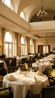 Elegant upscale restaurant dining room with arched windows, chandeliers, white tablecloths and formal table settings in warm beige interior design.