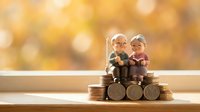 Elderly couple figurines sitting on stacks of coins representing retirement savings, pension planning and financial security for senior years.