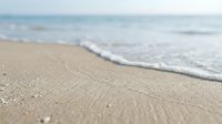 Soft ocean waves gently wash onto sandy beach shore with shallow depth of field, creating serene coastal landscape for travel, vacation, and relaxation themes.