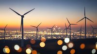 Wind turbines silhouetted against sunset sky with bokeh city lights creating renewable energy landscape for sustainable power generation concepts.