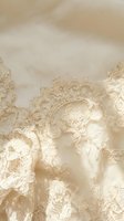Elegant champagne lace fabric with intricate floral patterns and delicate embroidery details on soft beige silk background for luxury fashion design.