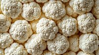 Fresh organic cauliflower heads arranged in rows creating natural pattern background. Close up view of white vegetable florets showing detailed texture.