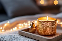 Glowing aromatic candle in decorative golden holder on wooden tray with soft bokeh lights creating cozy atmosphere for relaxation and meditation.