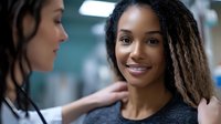 Young African American woman with dreadlocks smiling during medical consultation with female doctor in modern healthcare facility for wellness checkup.