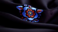 Vibrant blue and orange floral embroidery detail on black fabric showcases traditional folk art style with intricate stitching and decorative pattern design.