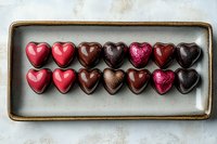 Heart-shaped chocolate pralines in different colors and textures arranged in two rows on ceramic plate. Romantic dessert concept for Valentine's day celebration.