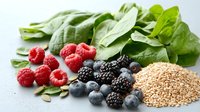 Fresh berries with spinach leaves and quinoa seeds on gray surface, healthy ingredients for nutritious breakfast bowl or smoothie preparation.