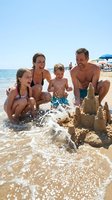 Family of four enjoying beach day building sandcastles in shallow ocean water. Parents with two children playing together during summer vacation at seaside resort.