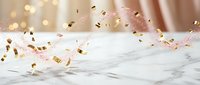 Festive golden and pink confetti falling on white marble surface with warm bokeh lights creating elegant celebration atmosphere for party events.