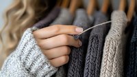 Close up of female hands sewing and repairing warm knitted sweaters in neutral colors. Sustainable fashion and clothing care concept showing mending technique.