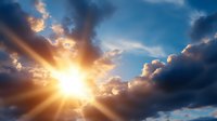 Dramatic sunset sky with bright sunburst breaking through dark storm clouds, creating golden rays and atmospheric light beams against deep blue background.
