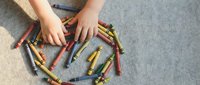 Child hands organizing colorful crayons in circle pattern on carpet floor for creative art project and educational drawing activities.