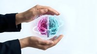 Male hand holding glowing split brain illustration in pink and blue, representing left and right hemisphere, creativity and logic, innovation and analytical thinking concept.