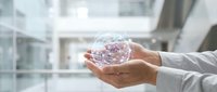 Hands holding transparent globe with digital network connections in modern office environment, representing global business, technology innovation, and worldwide communication.