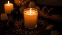 Warm glowing candles create cozy atmosphere with coffee beans and wooden spoons on dark surface for relaxation and aromatherapy spa treatments.