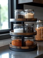 Tiered wooden and metal spice rack with glass jars containing various cooking ingredients like salt, pepper, and spices, organized on kitchen counter near window.