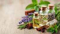 Essential oils in glass bottles with lavender, herbs and spices on wooden background for aromatherapy, wellness and natural healing treatments.