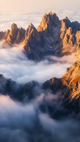 Dramatic mountain peaks emerging from sea of clouds at golden hour sunrise with warm light illuminating rocky summits and misty valleys below.