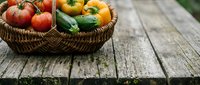 Fresh red apples and yellow bell peppers in woven basket on rustic wooden table, ideal for farmers market, organic produce, and food styling projects.