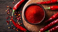Ground red chili powder in rustic bowl surrounded by whole dried red chili peppers and scattered peppercorns on dark wooden background, spicy seasoning.