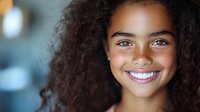 Young African American woman with natural curly hair and bright white smile against blurred background, radiating joy and confidence in casual portrait.