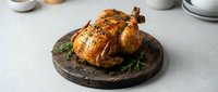 Golden roasted whole chicken with herbs on rustic wooden board, perfect for holiday meals, family dinners, and culinary presentations.