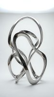 Modern abstract metal sculpture with flowing curved ribbons in silver chrome finish on white background for contemporary interior design and art decoration.