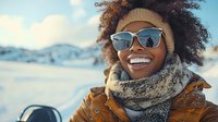 Young woman with curly hair and dark skin wearing sunglasses and winter clothing smiles outdoors in snowy landscape. Winter portrait for seasonal campaigns and lifestyle content.