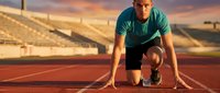 Focused athlete in starting position on running track during golden hour sunset, ready to sprint in stadium setting for sports and fitness concepts.