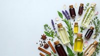 Essential oils collection with fresh herbs, spices and amber bottles on white background for aromatherapy, natural wellness and holistic healing treatments.