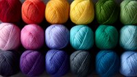 Colorful yarn balls arranged in rows showcasing vibrant spectrum from pink to red, yellow, green, turquoise and blue tones. Soft wool threads for knitting and crochet projects.