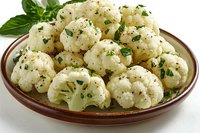 Steamed cauliflower florets seasoned with herbs, black pepper and parsley served on brown ceramic plate with fresh basil garnish, healthy vegetarian side dish.