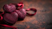 Red glittery heart decorations with satin ribbon on dark rustic background. Romantic holiday composition with sparkly ornaments and copy space.