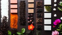 Culinary flat lay with various tea types, spices, and edible flowers arranged in geometric pattern on dark background. Fresh herbs and aromatic ingredients.