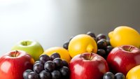 Fresh colorful fruits including red apples, green apple, oranges and dark grapes arranged together on neutral background for healthy eating concepts.