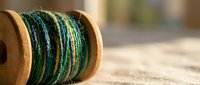 Wooden spool with colorful green and blue embroidery thread for needlework and crafting projects on rustic wooden surface.