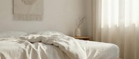 Unmade bed with white linens, natural light from window, minimalist bedroom interior with neutral tones, suitable for home decor and lifestyle content.