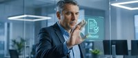 Mature male professional in dark blazer and light shirt touches chin thoughtfully in modern office with approval icon on glass panel, representing business decision-making and corporate success.