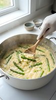 Cooking creamy risotto with green beans in white pot by window, wooden spoon stirring Italian rice dish with fresh vegetables.