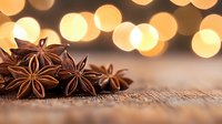 Star anise pods on rustic wooden surface with warm glowing bokeh lights in background, creating cozy holiday atmosphere for seasonal cooking and decoration.