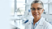 Professional African American female dentist with glasses smiling in modern dental office clinic wearing white coat for healthcare and medical services.