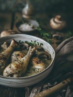 Roasted chicken drumsticks with herbs in ceramic dish on rustic wooden table. Homemade comfort food cooking concept for family dinner preparation.