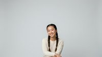 Young Asian woman with long dark braided hair wearing a cream-colored cardigan, smiling at camera against neutral background. Suitable for business, lifestyle, and portrait projects.