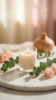 Burning candle in glass surrounded by eucalyptus leaves and pink salt crystals on marble tray creating peaceful spa atmosphere for relaxation and wellness.