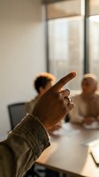 Dark-skinned hand pointing finger during diverse business meeting in modern office, colleagues listening at conference table in warm light.