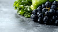 Fresh dark purple grapes with water drops on gray concrete background, selective focus. Green grape bunch and parsley leaves create natural composition.