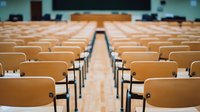 Empty wooden chairs arranged in rows inside lecture hall with selective focus on center aisle, creating symmetrical perspective view for education and learning concepts.