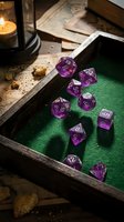 Purple translucent polyhedral dice set arranged on green felt gaming surface with wooden tray, candle, and vintage maps for tabletop role-playing games and fantasy gaming sessions.