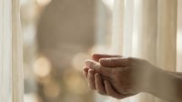 Elderly person holding hands with younger individual by window with soft natural light and blurred background, conveying care and intergenerational connection.